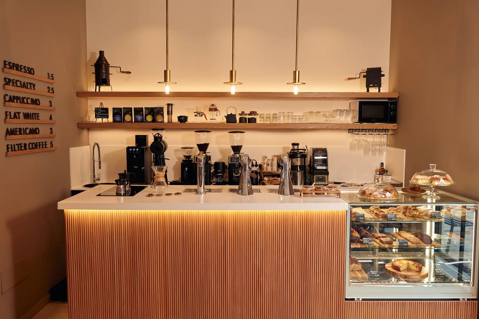 The counter at Morettino Bottega with V60 drippers, grinders, and a pastry case lit by hanging brass lamps