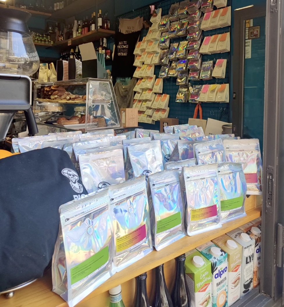 The retail shelf at Vago Rizzuto lined with bagged specialty coffee, oat and coconut milk cartons, and the shop's grinder