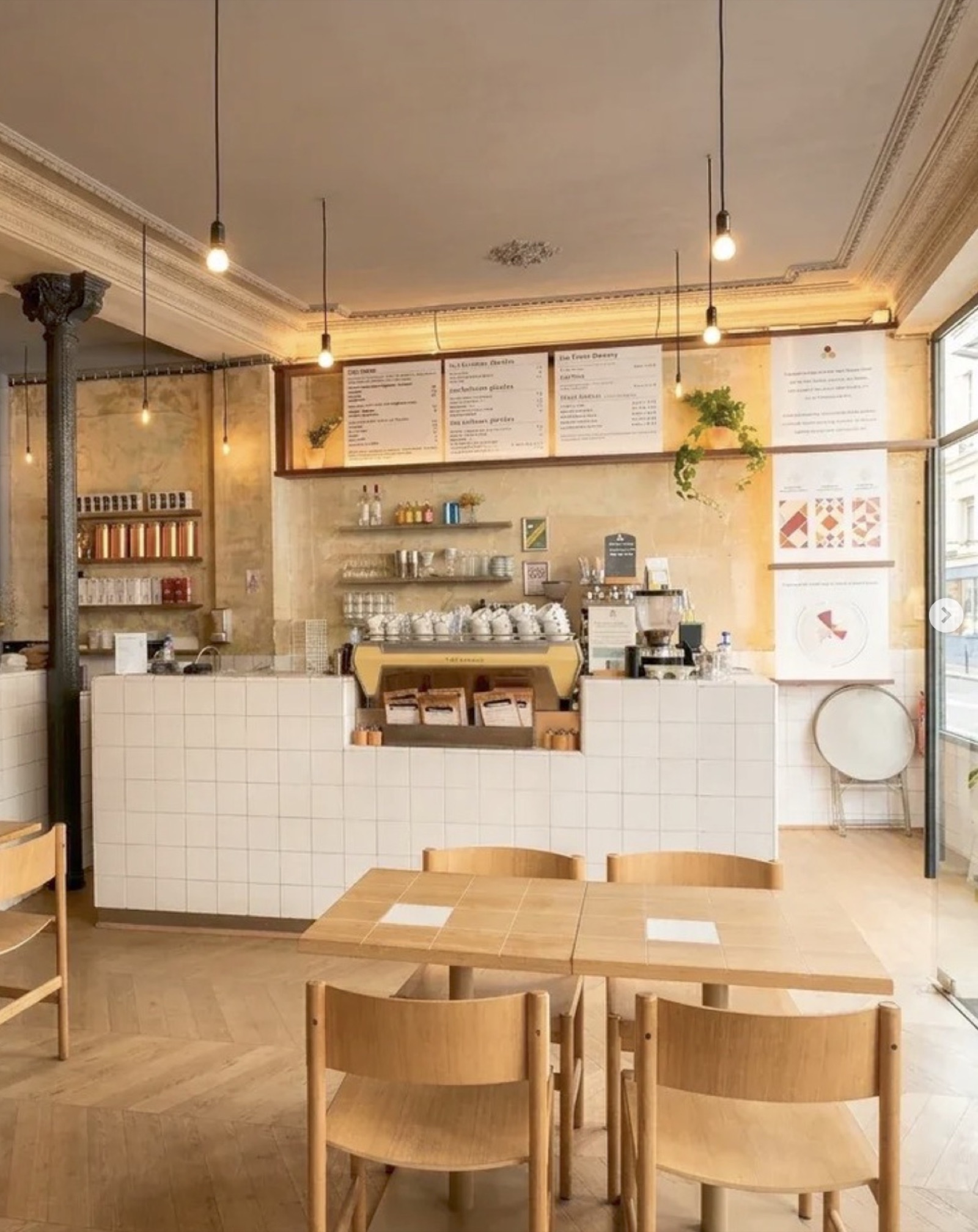 The white-tiled counter at Coutume Café, espresso machine and bagged beans below the menu boards, wood tables in front