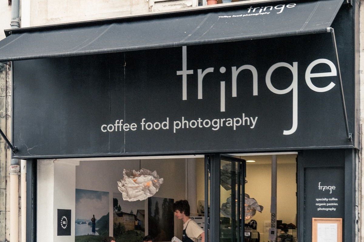 The black Fringe awning with its coffee food photography tagline, gallery prints and a paper cloud light fixture visible through the open storefront