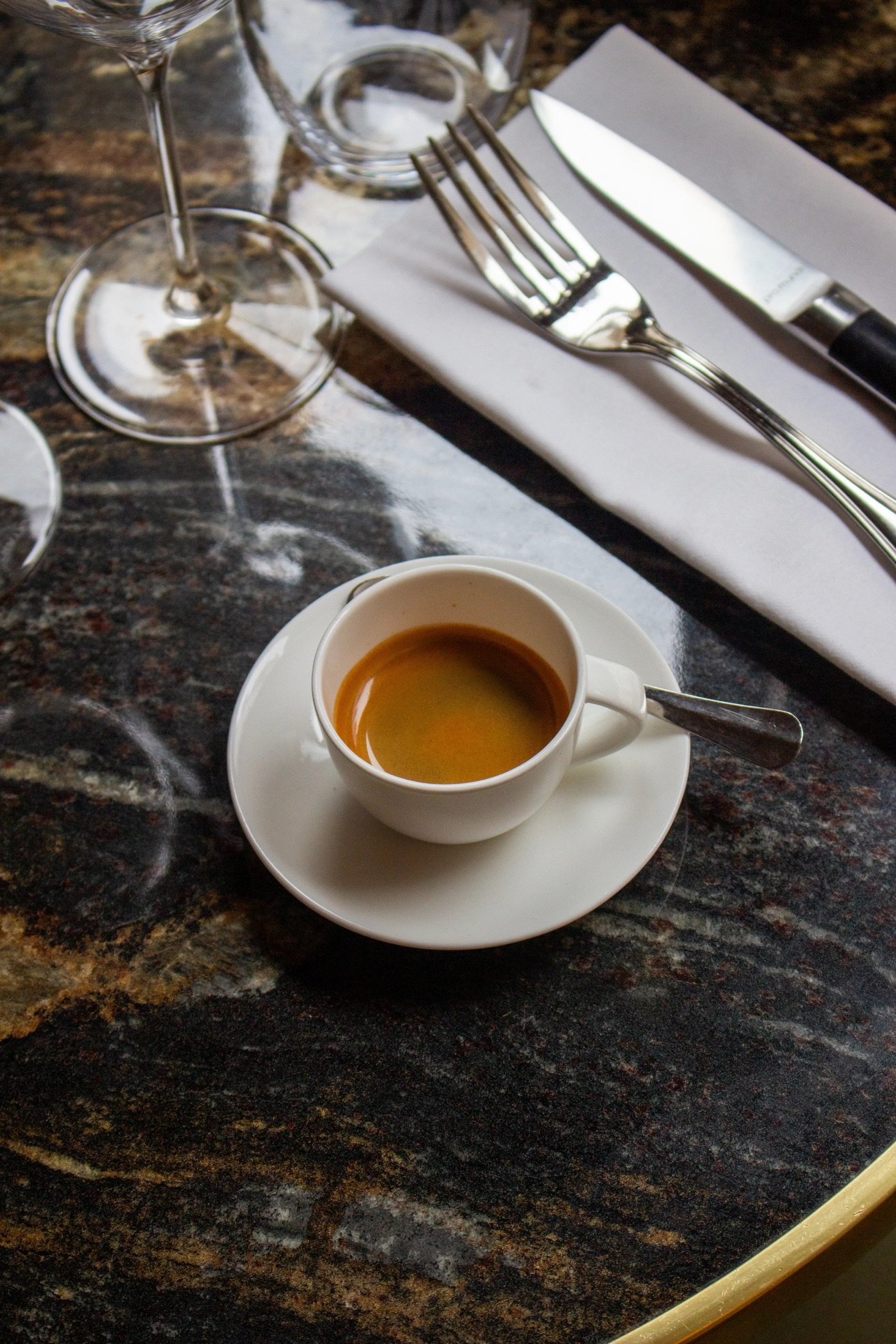 An espresso on a marble table setting at Café Lomi, cutlery and a wine glass beside it