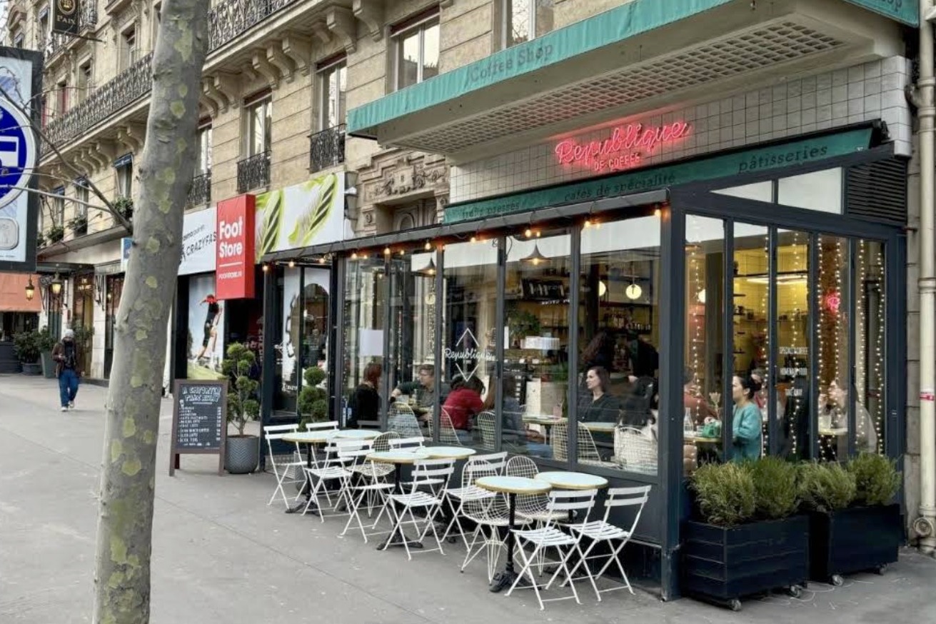 The République of Coffee storefront, a neon République de Coffee sign glowing above a glass fronted terrace with string lights and outdoor tables