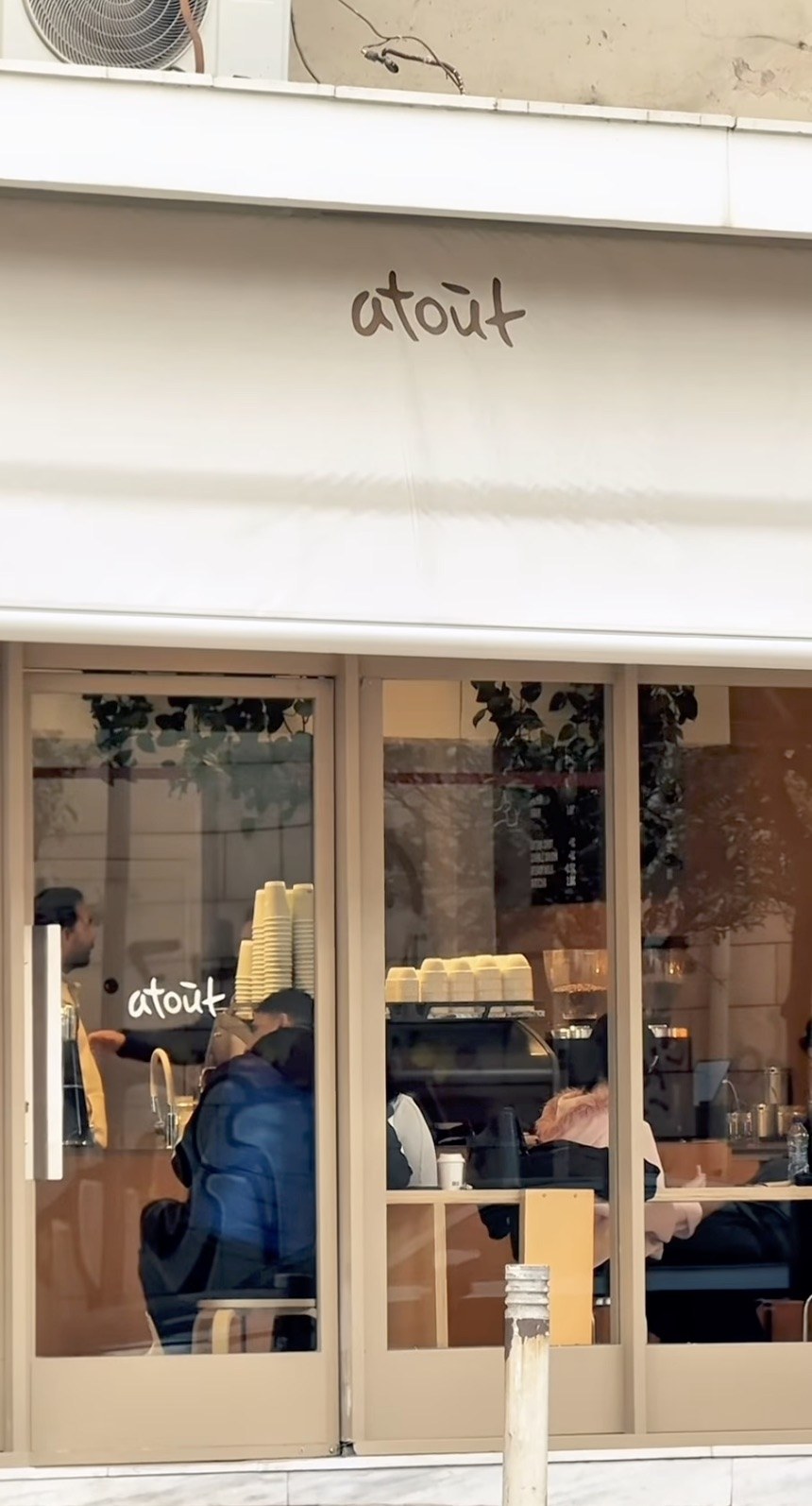 The Atout storefront seen through the glass frontage, the espresso bar and seating visible inside beneath the corner awning