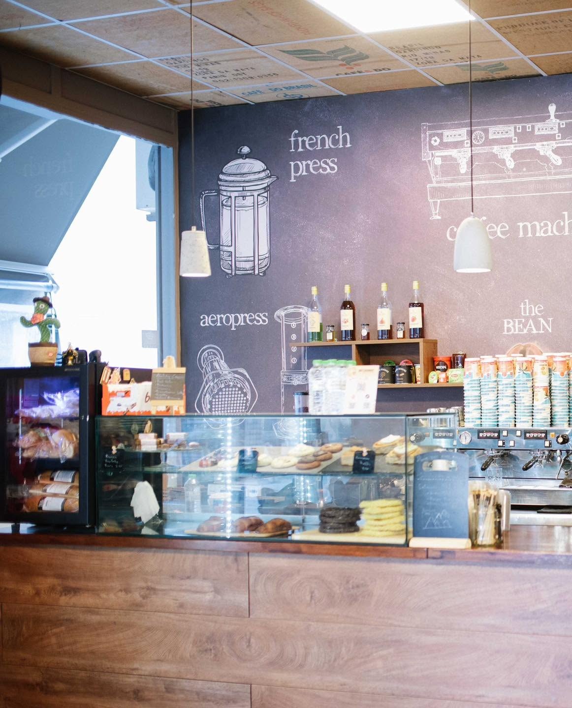 A pastry case beneath a chalkboard wall illustrated with a french press, aeropress and espresso machine
