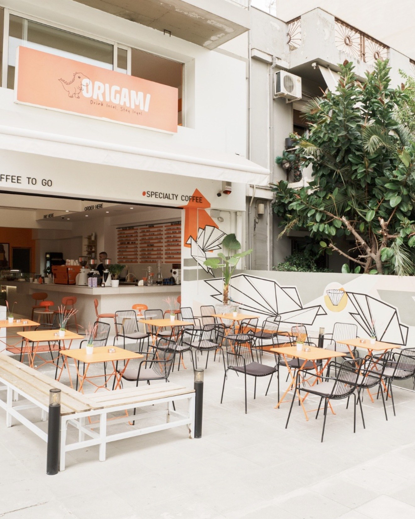 The Origami storefront and outdoor terrace, orange bistro tables and black wire chairs beneath an origami dove mural