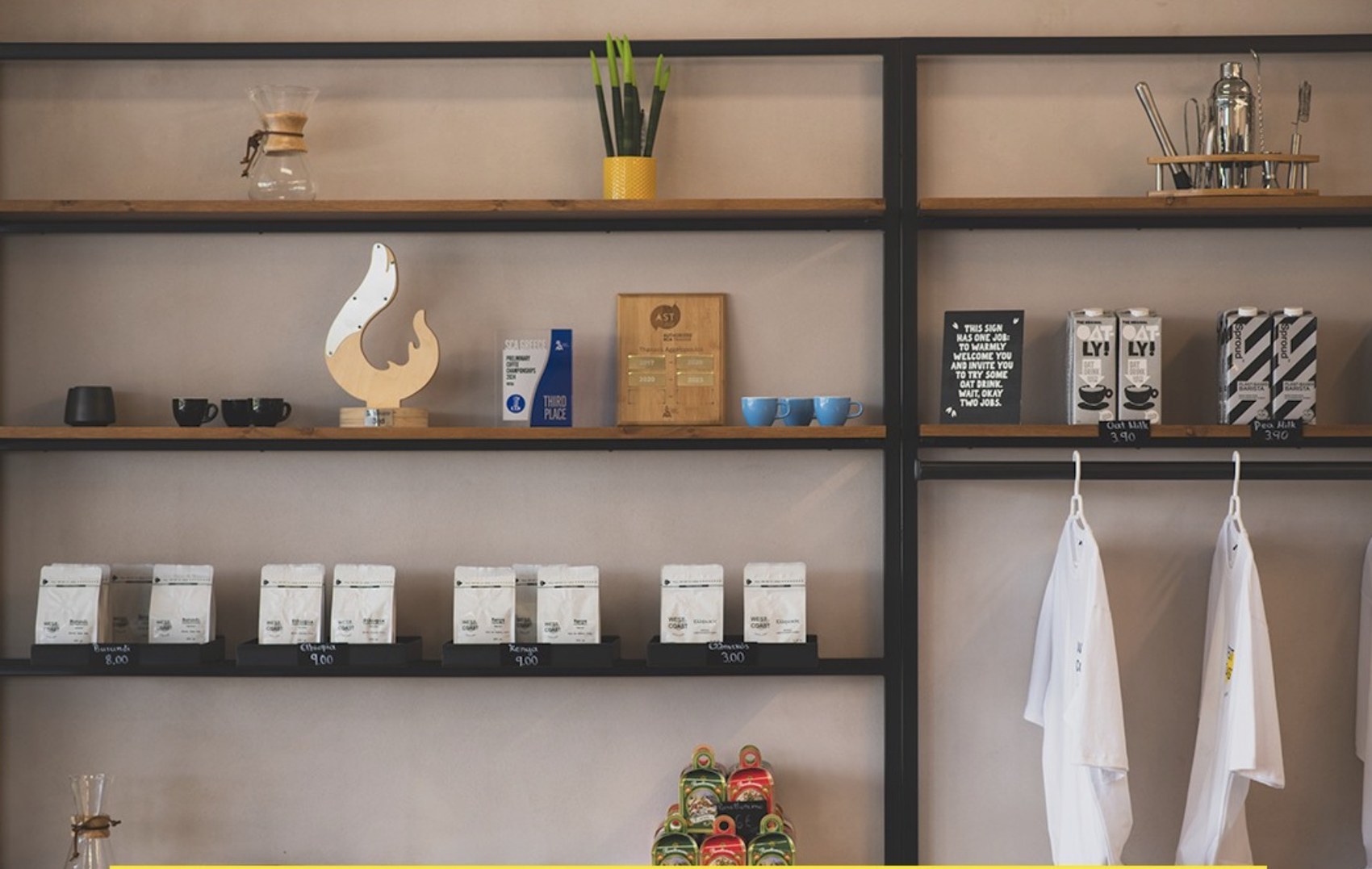 A shelving unit with branded West Coast retail bean bags, brewing equipment and a coffee competition award plaque