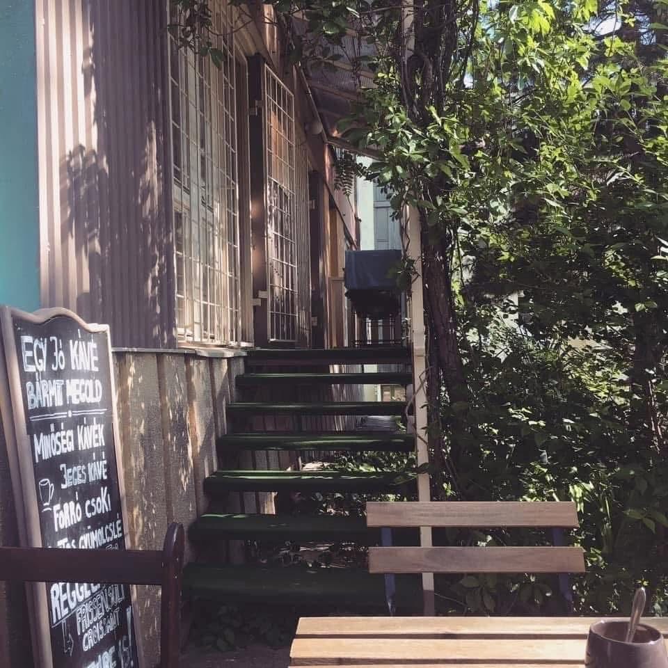 A chalkboard coffee menu beside a green staircase leading up through greenery at Block Coffee Room