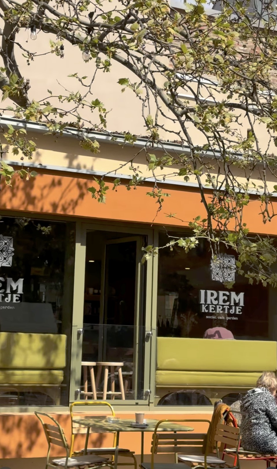 The Irem Kertje storefront with its social cafe garden signage, a to go coffee cup on an outdoor table below