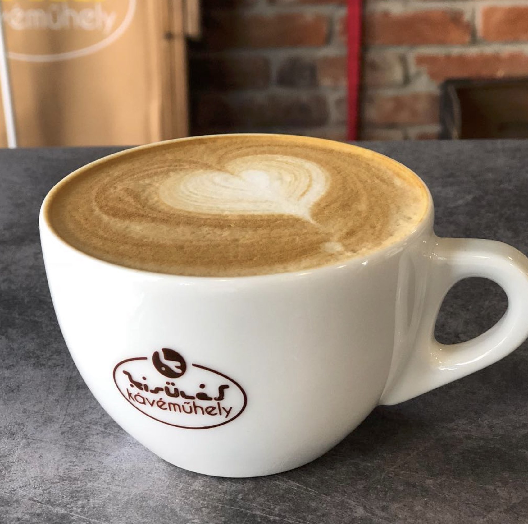 A branded Kisülés Kávéműhely cup with heart shaped latte art