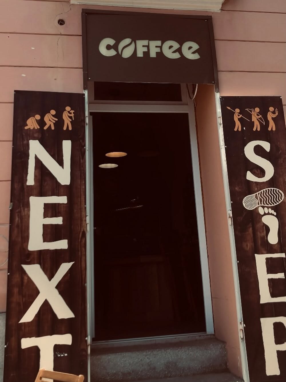 The entrance to Next Step Coffee, with a coffee bean sign above the door and evolution themed lettering on either side
