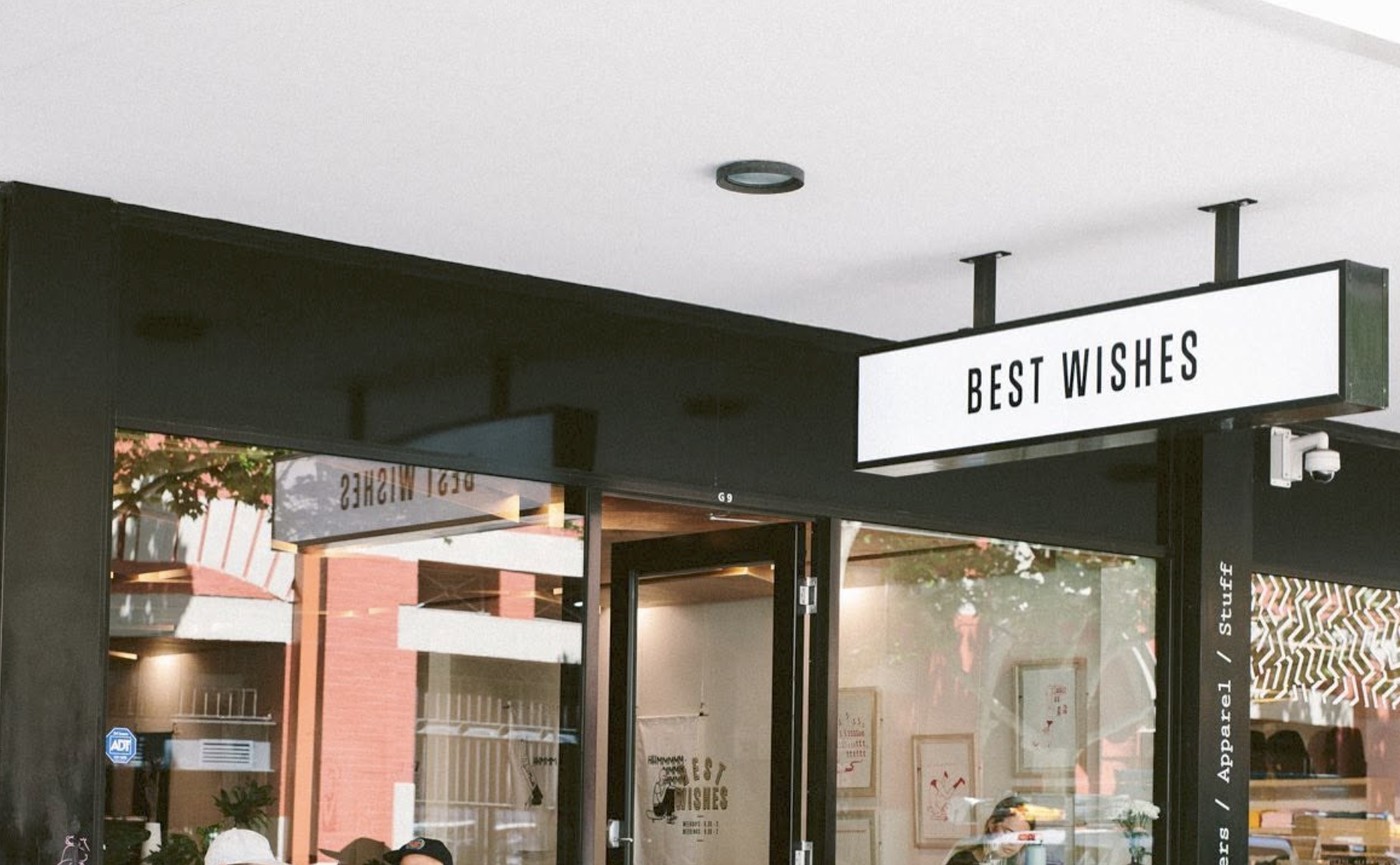 The Best Wishes sign mounted above the storefront entrance, with the shop's window signage visible behind the glass