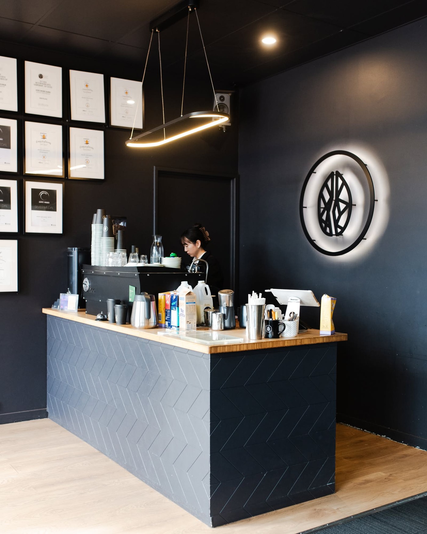 The black tiled counter and espresso bar at Blacklist's Welshpool roastery, framed award certificates on the wall and a barista working behind the machine