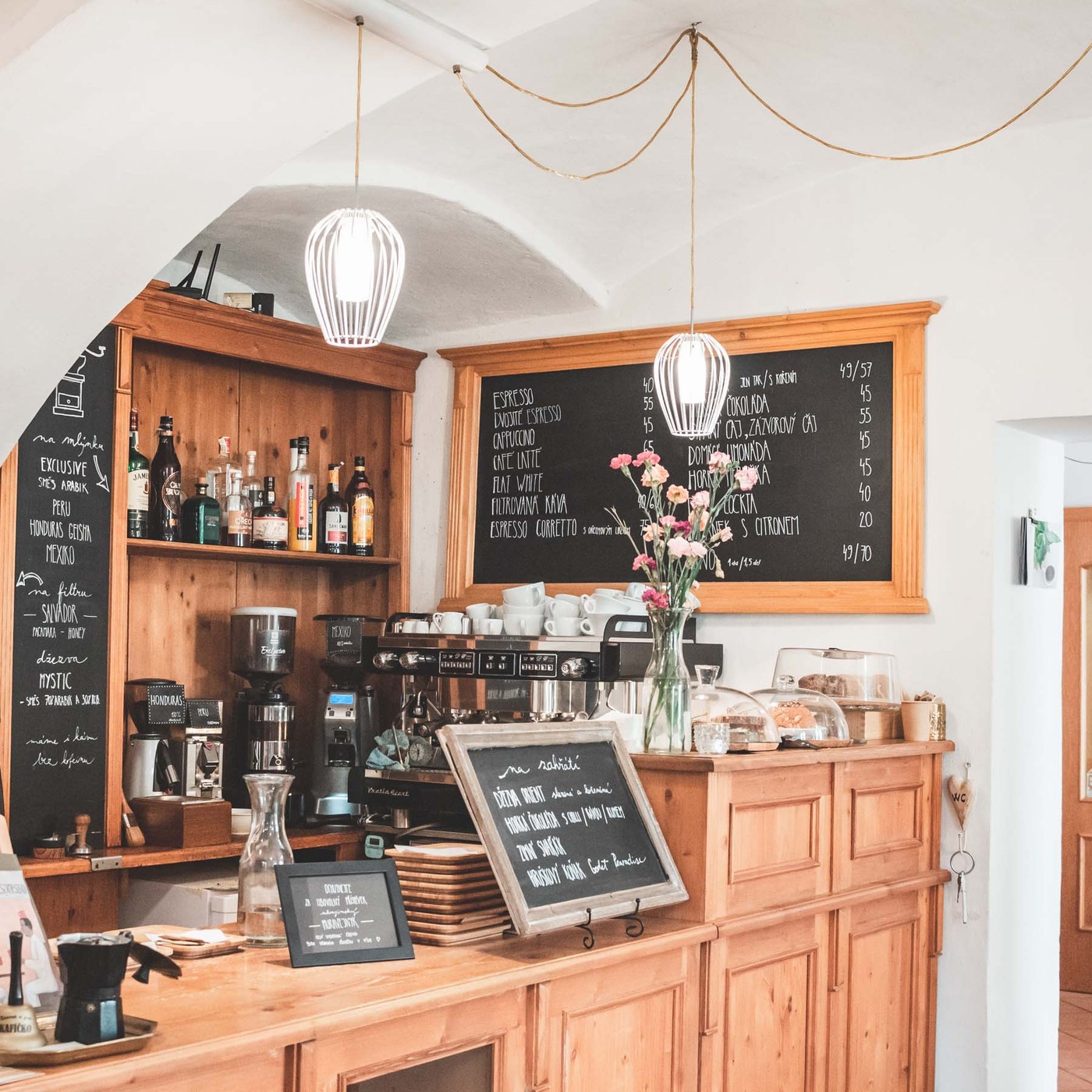 Orient Coffee's wood-paneled counter with an espresso machine, hanging cage pendant lights, a chalkboard menu, and fresh flowers on the bar