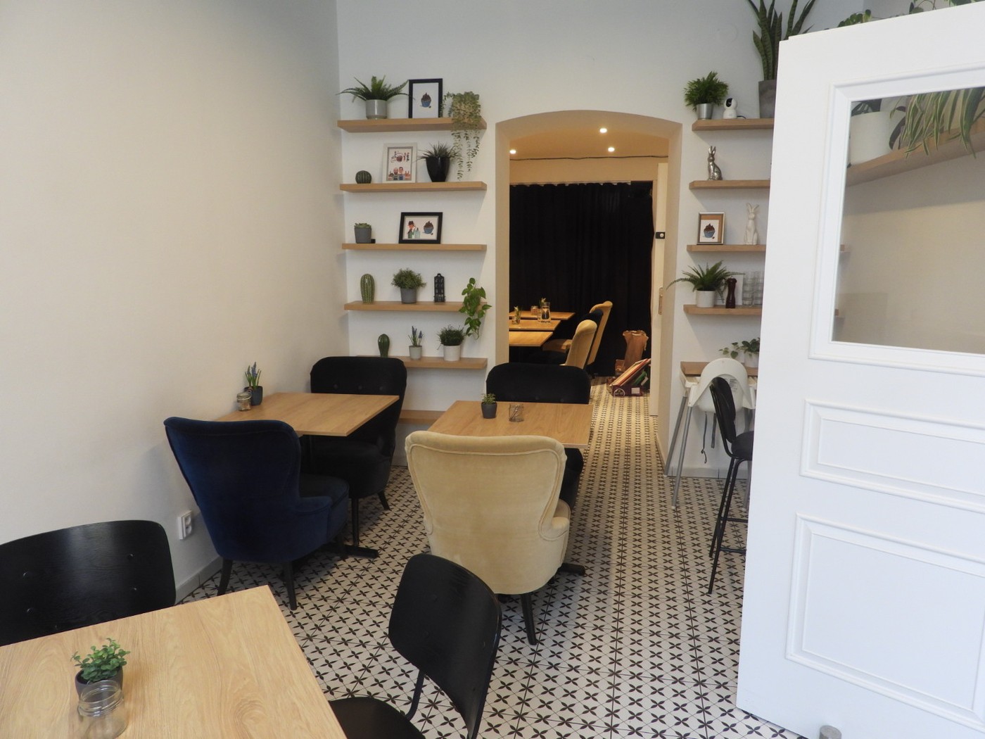 The small tiled dining room at Pappa Coffee, with wingback armchairs, wooden tables, and shelves of plants and decor beside an arched doorway