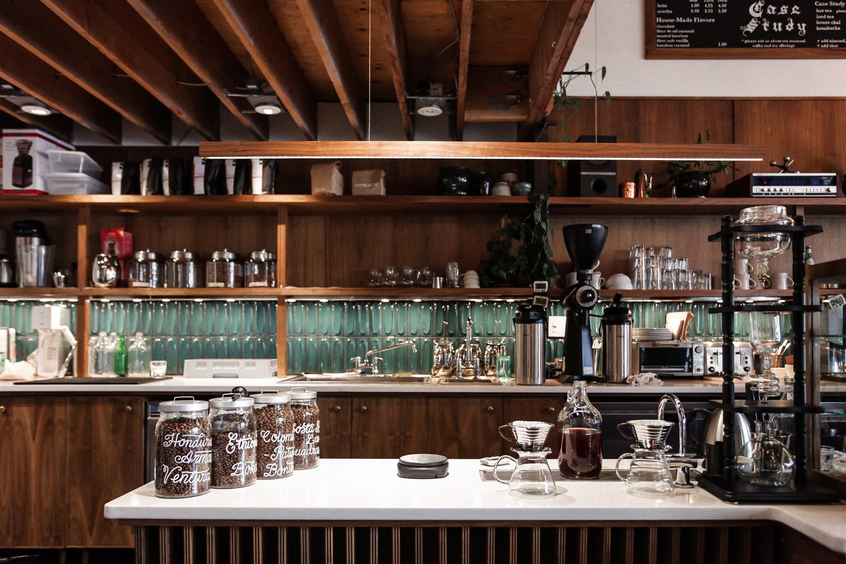 The wood shelved coffee bar at Case Study, labeled bean jars, a batch brewer and pour-over glassware on a white counter