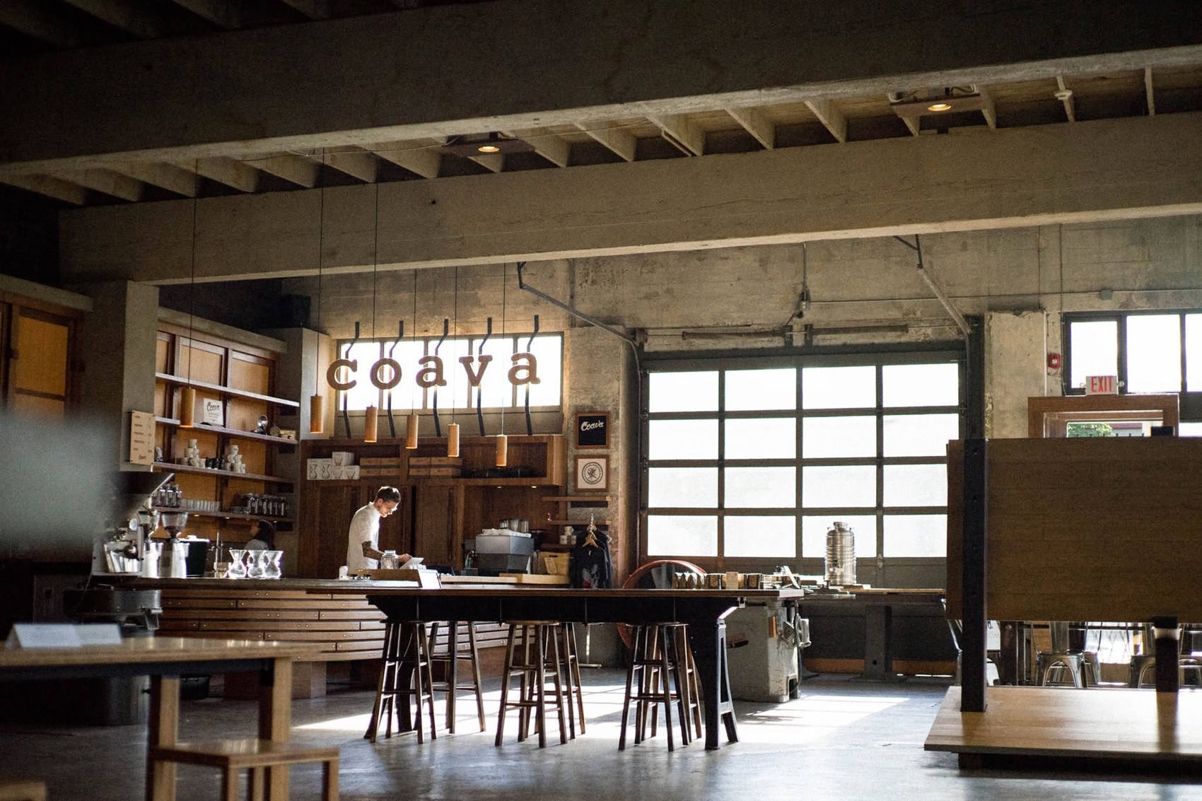 The Coava sign hanging above the wooden bar inside the Grand Avenue cafe, communal tables and a garage door window in view