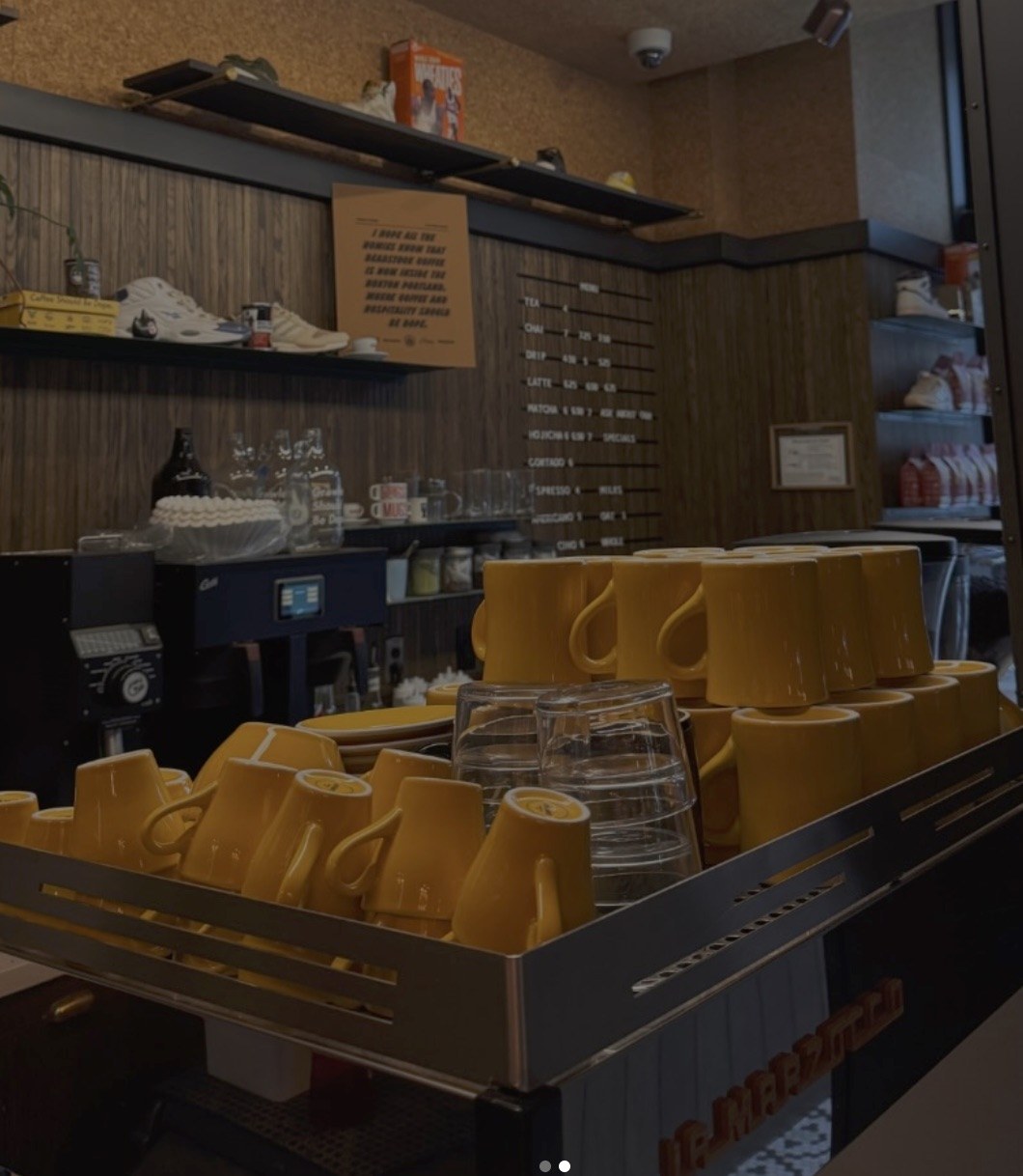 Stacked mustard yellow mugs and glassware on the espresso bar, sneaker boxes and shoes displayed on shelves above