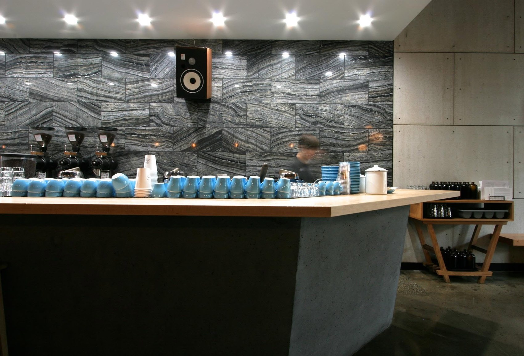Rows of pale blue cups lined up on the timber and concrete espresso bar against a striated grey stone wall