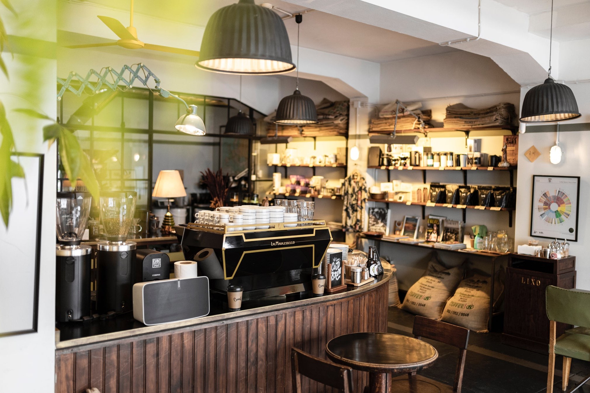 The curved dark wood bar at Combi in Bonfim, a La Marzocco machine, grinders and shelves of beans and brewing gear behind it