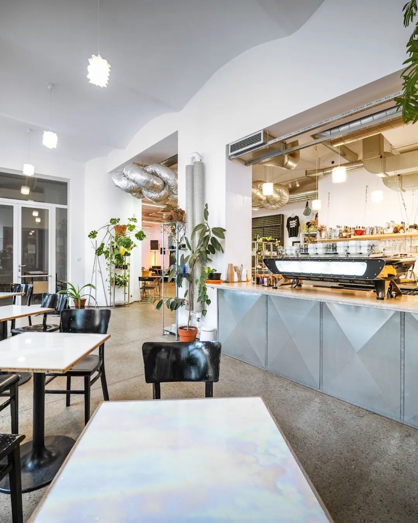 The industrial dining room at Acid Coffee, exposed ductwork and plants around a diamond patterned counter