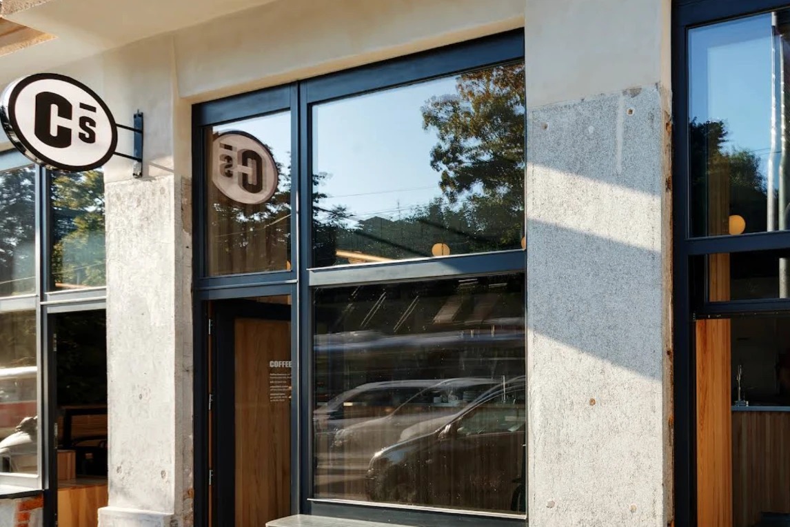 The Coffee Source storefront with its round C S logo sign and COFFEE lettering on the door, wooden counter visible inside