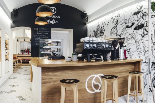 The wood counter and espresso bar at Dos Mundos Letna with a hand drawn coffee mural covering the wall behind it