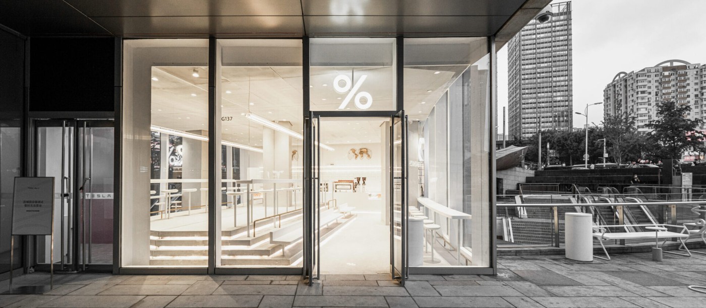 The glowing white storefront entrance with a lit up percent sign above the door and G137 marked on the glass
