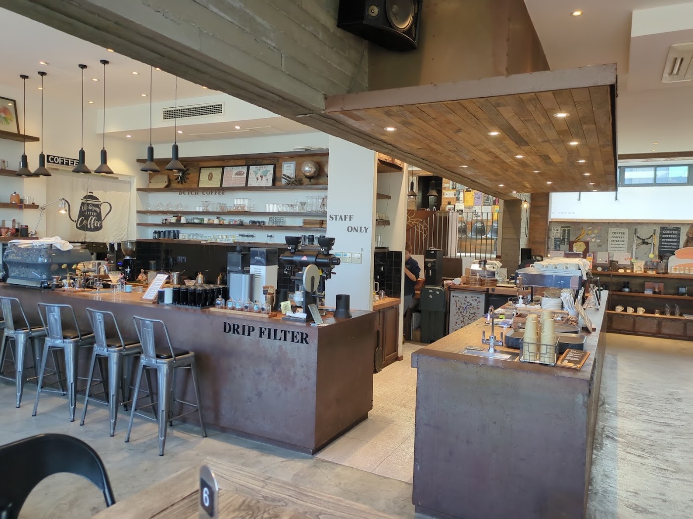 The drip filter bar at Vanilla Specialty Coffee, with an espresso machine, rows of grinders and glass canisters, and hanging pendant lights under a wood ceiling panel