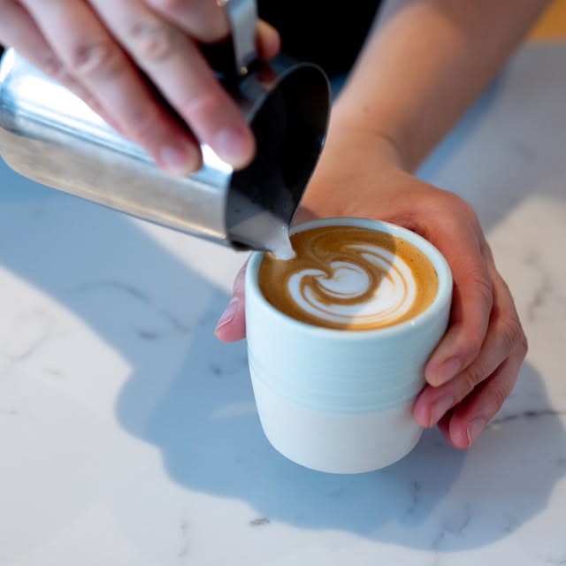 A barista pouring latte art into a pale blue cup at Kaffi Ó-le