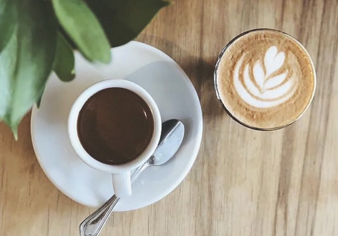 An espresso beside a cappuccino with leaf latte art on a wooden table at Kaktus Espressobar