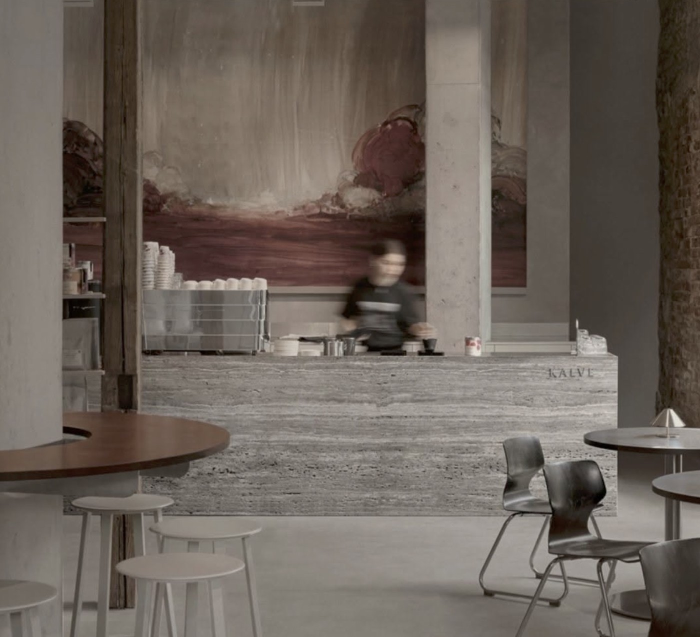 The stone KALVE counter with a motion blurred barista at work beneath a large abstract painting in muted red and grey