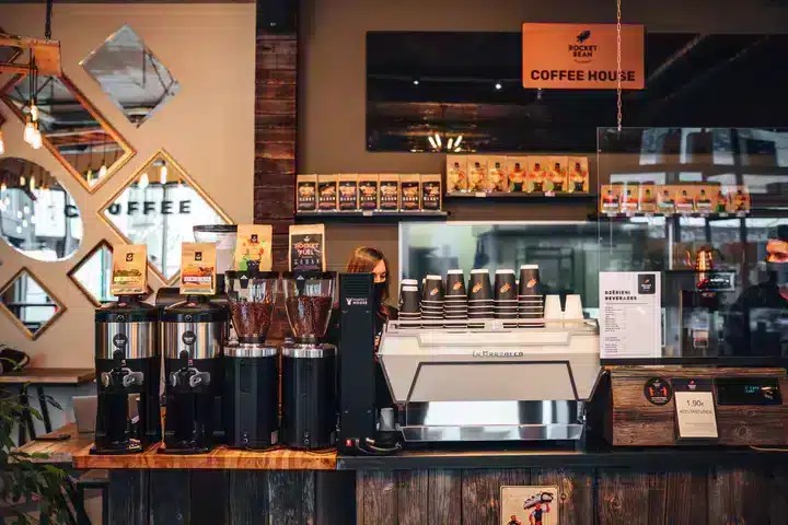 Rocket Bean's retail coffee bags and stacked branded cups beside the La Marzocco espresso machine, with a Coffee House sign on the wall