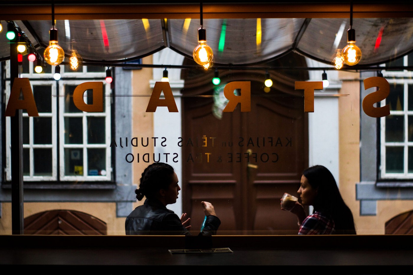 The reversed STRADA window lettering and string lights above two silhouetted customers seated at the counter