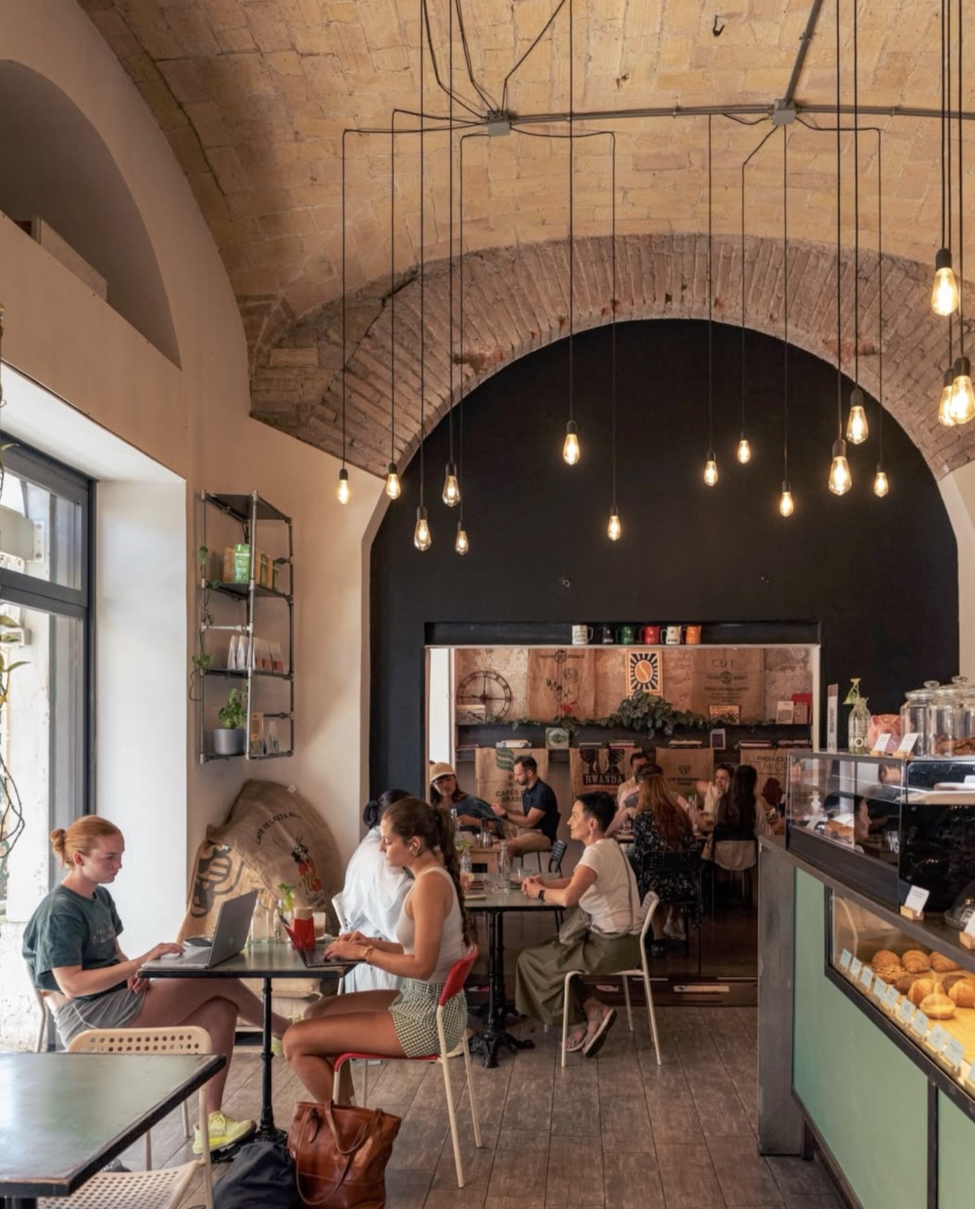 The vaulted brick-and-black-arch dining room at Sensorio Coffee Lab, pendant bulbs hanging above tables and a mint-green pastry case by the counter