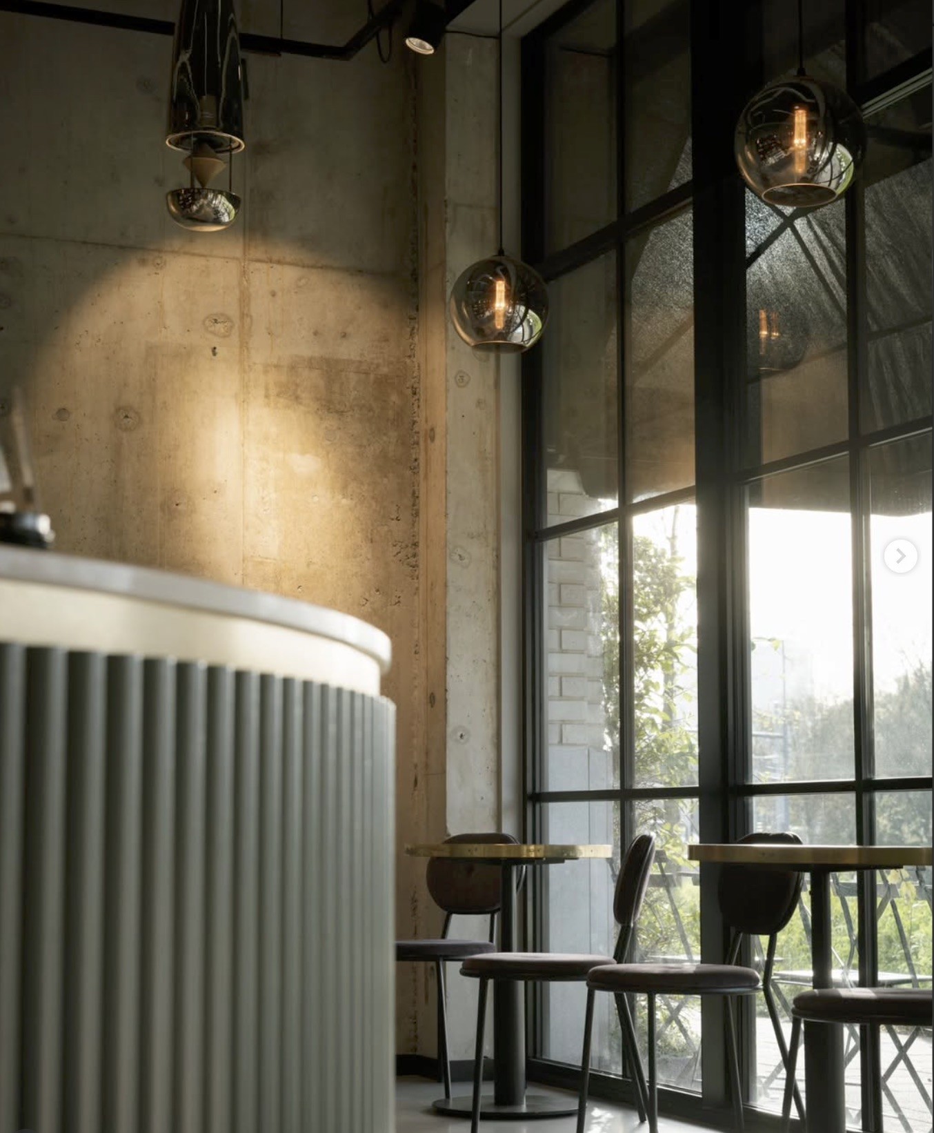 Globe pendant lights over a concrete counter beside floor to ceiling windows and cafe tables at Sound Kitchen