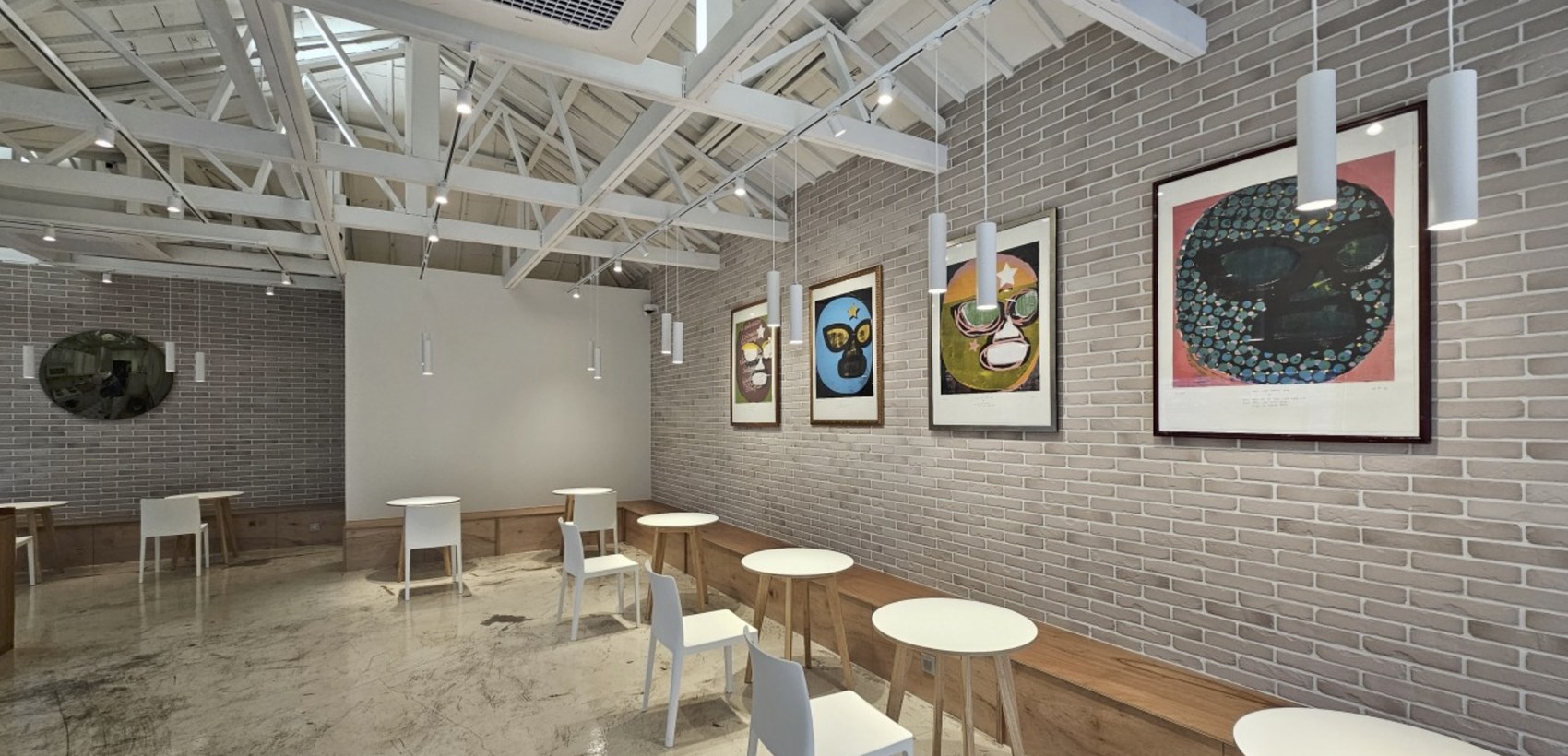 The renovated interior of Coffee Libre Yeonnam, exposed brick hung with colorful pop art masks above white cafe tables and a vaulted white ceiling