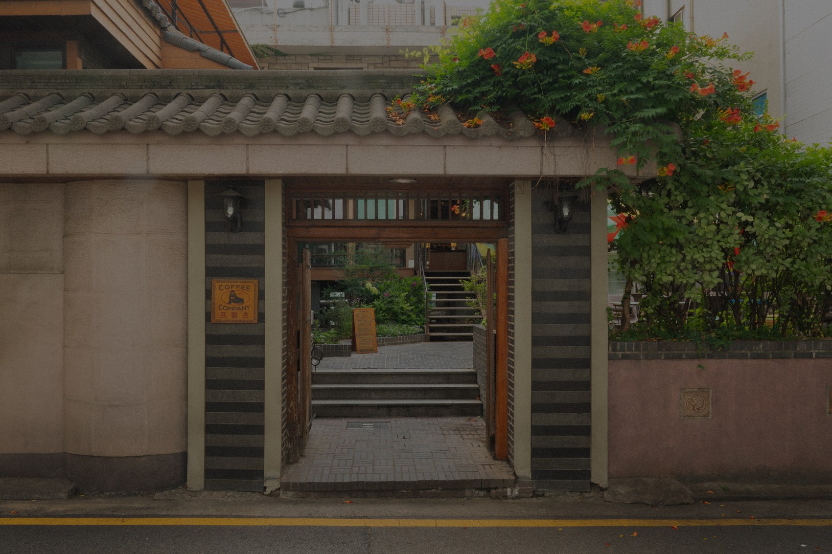 The tiled hanok gate entrance to Fritz Coffee Company's Dohwa branch, a seal-logo sign on the pillar and a courtyard with steps beyond