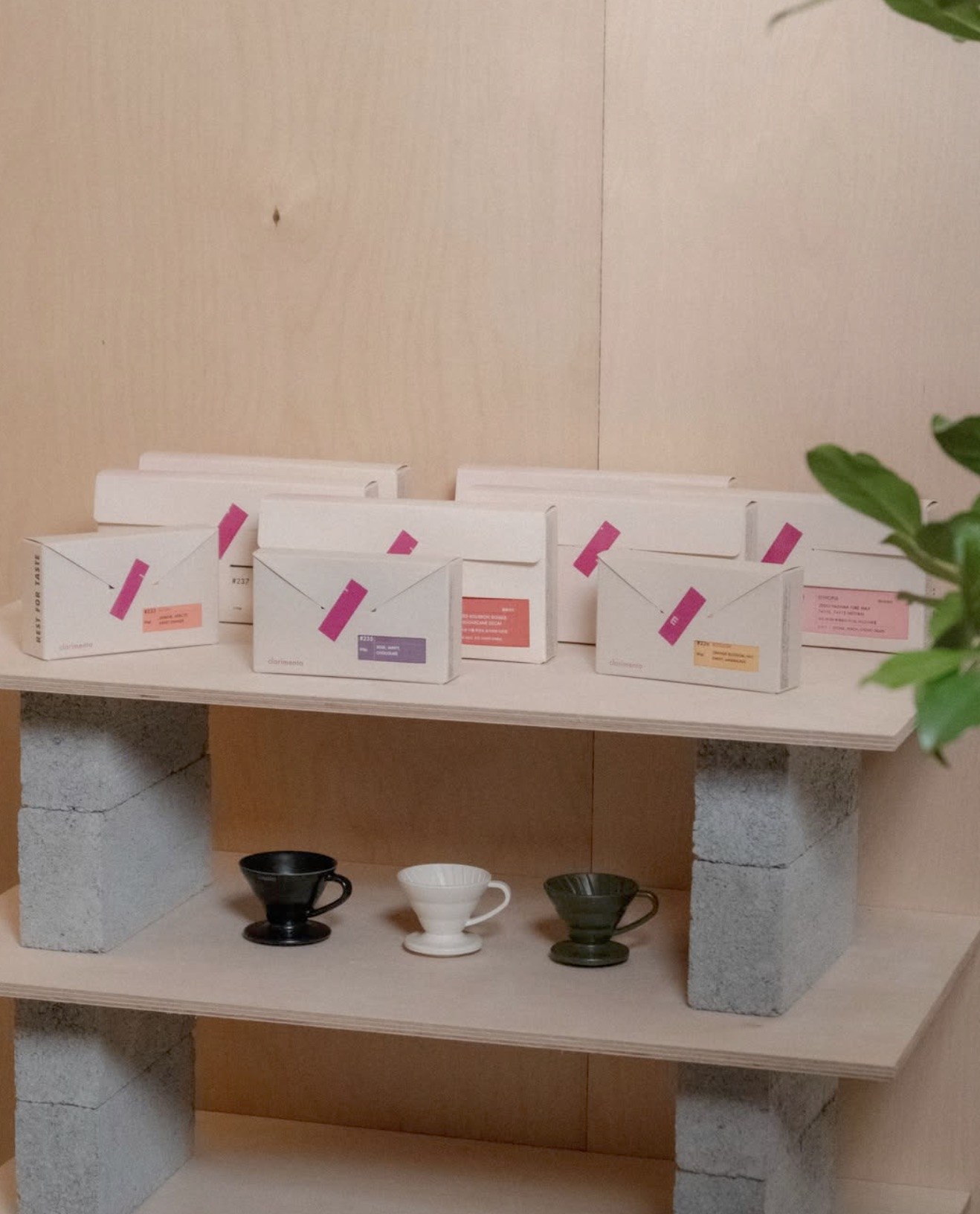 Retail bags of Clarimento coffee lined up on a plywood and concrete block shelf above a row of V60 drippers