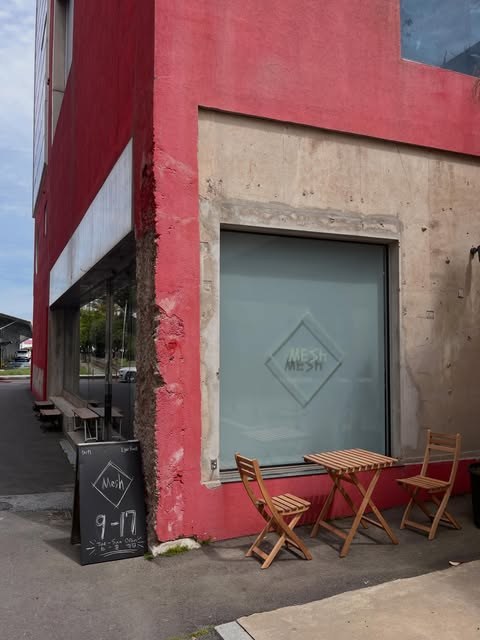 The MESH diamond logo etched on the storefront window above a small outdoor table and chairs