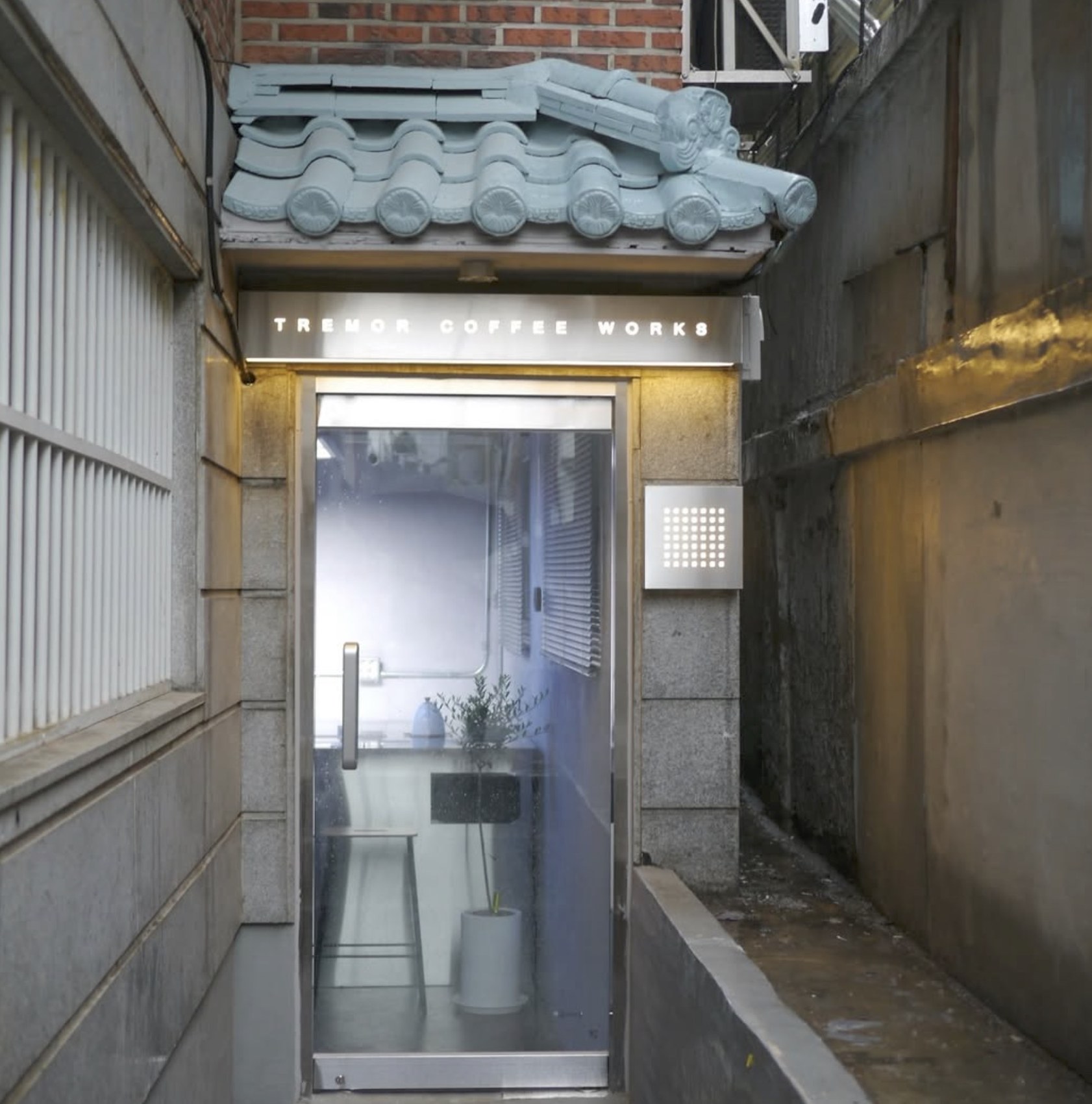 The alley entrance to Tremor Coffee Works, a traditional tiled roof over a steel and glass door with the shop's sign lit above