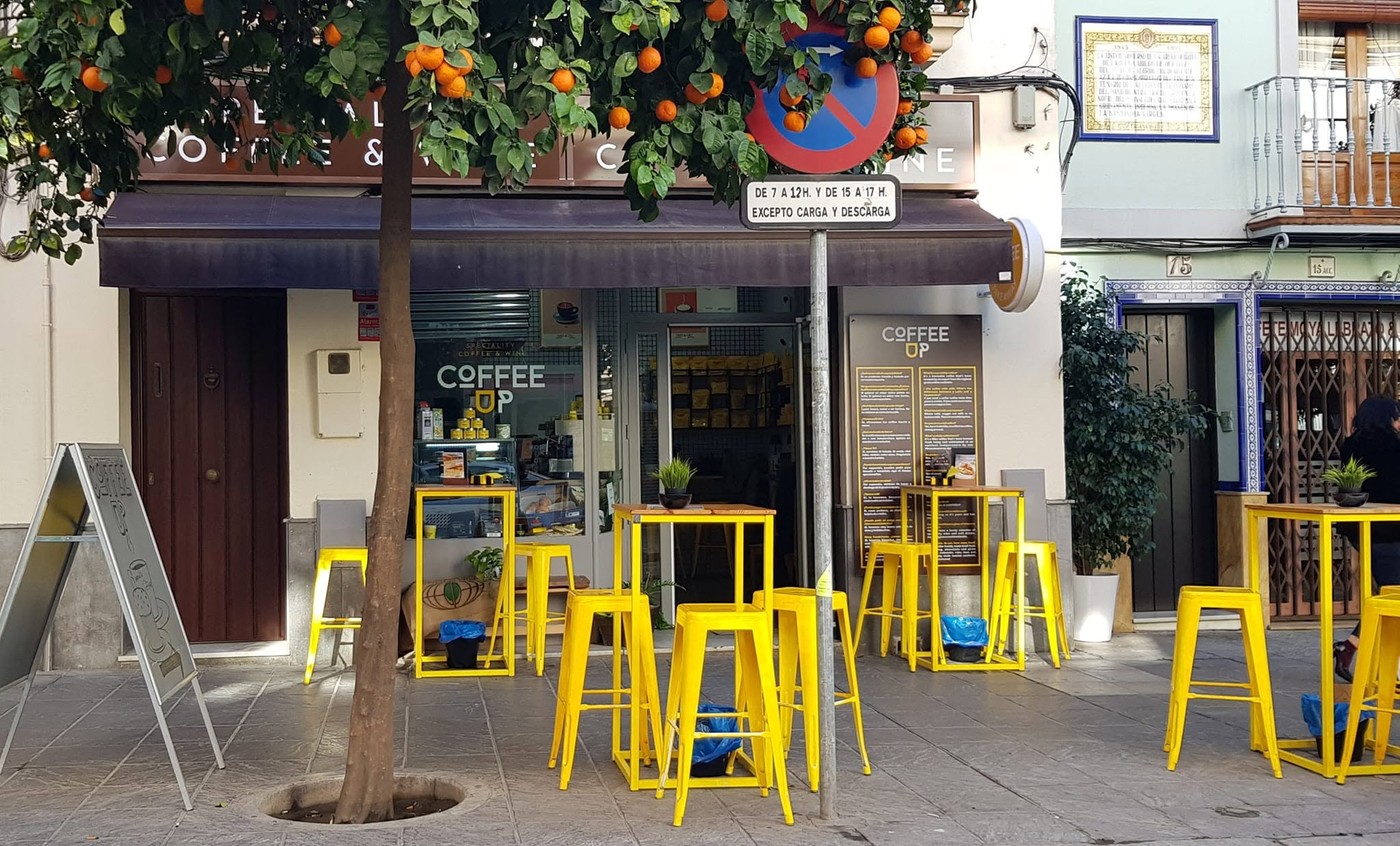 The Coffee Up storefront with yellow stools and tables under an orange tree, signage reading Coffee Up in the window
