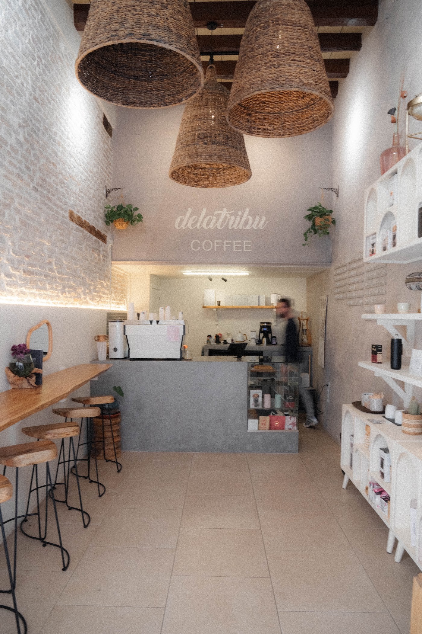 The delatribu COFFEE wall lettering beneath woven pendant lamps, with a concrete counter and espresso machine below