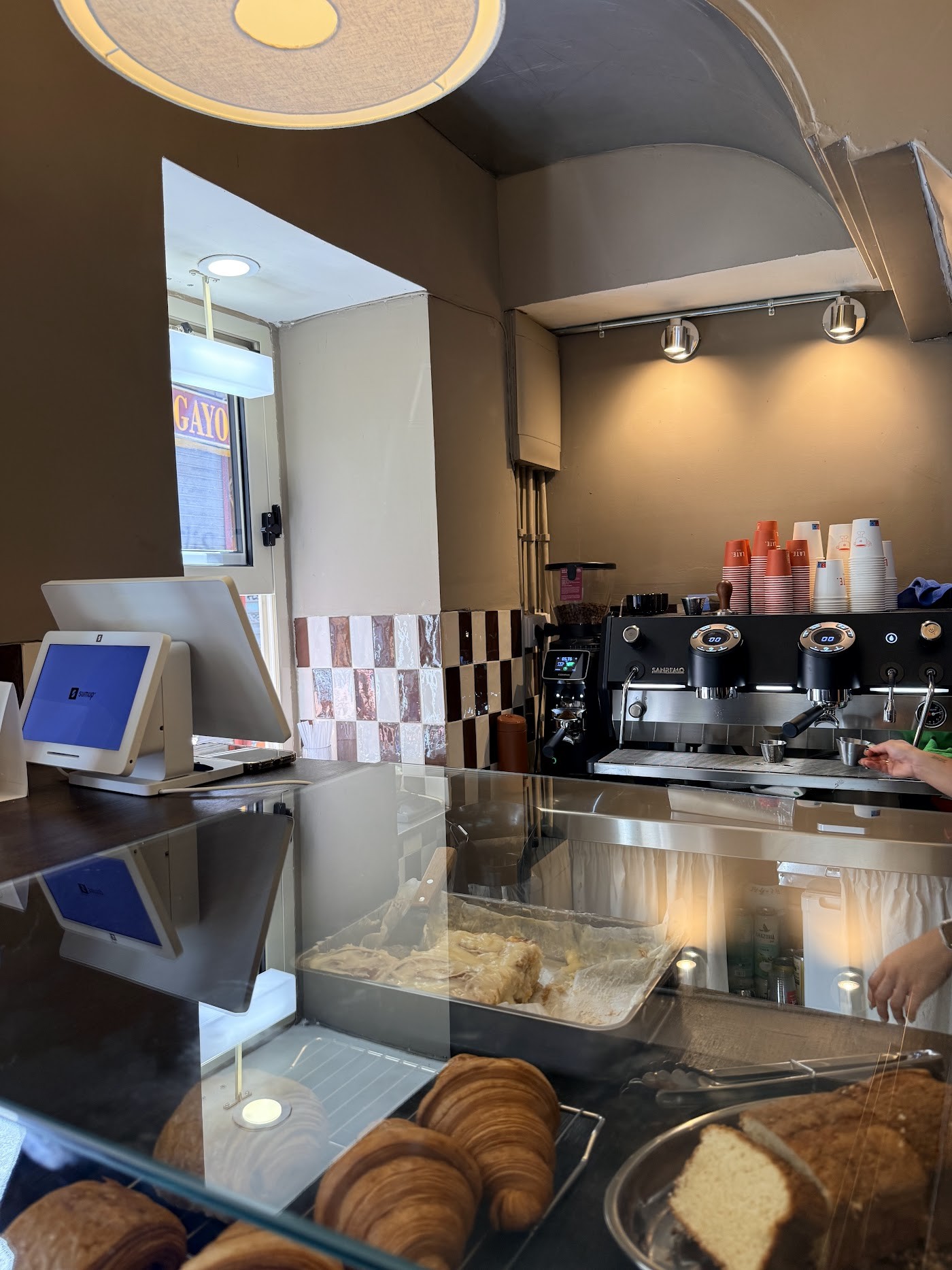 The LATE espresso counter with stacked branded takeaway cups, a pastry case of croissants, and warm pendant lighting