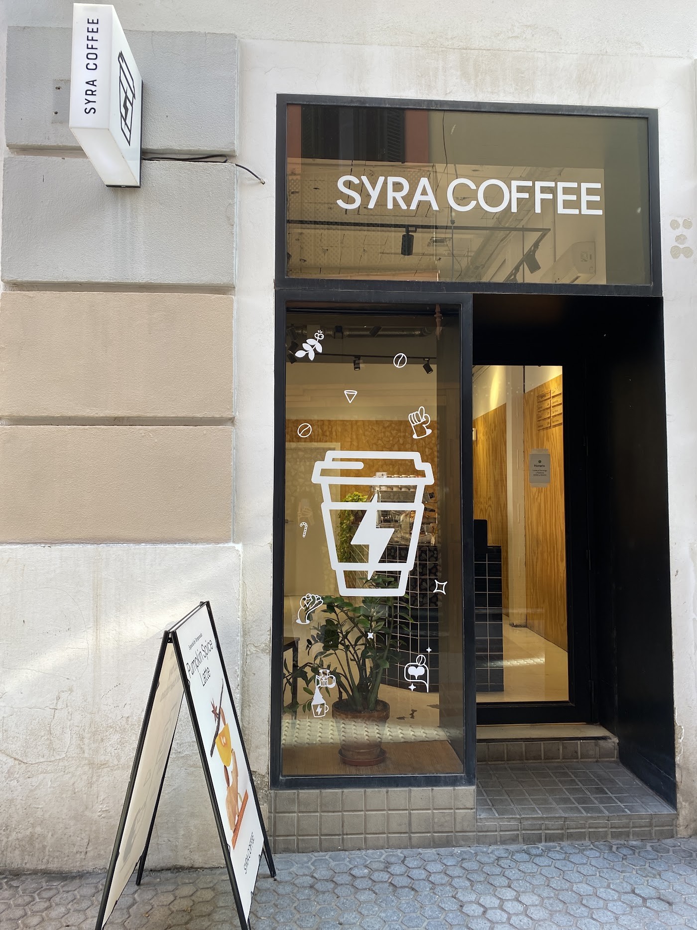 The minimalist SYRA COFFEE storefront with a branded cup decal on the window and a sandwich board out front
