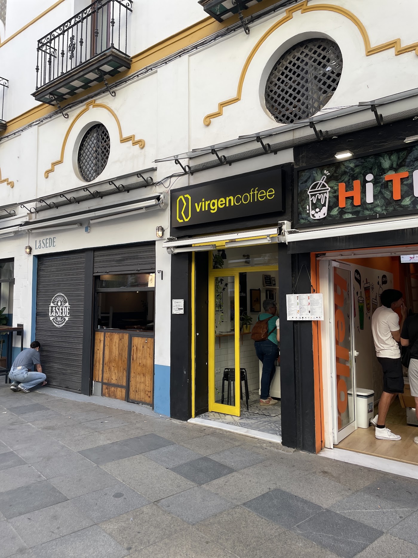 The yellow and black virgencoffee sign above the narrow storefront entrance on a Seville street corner