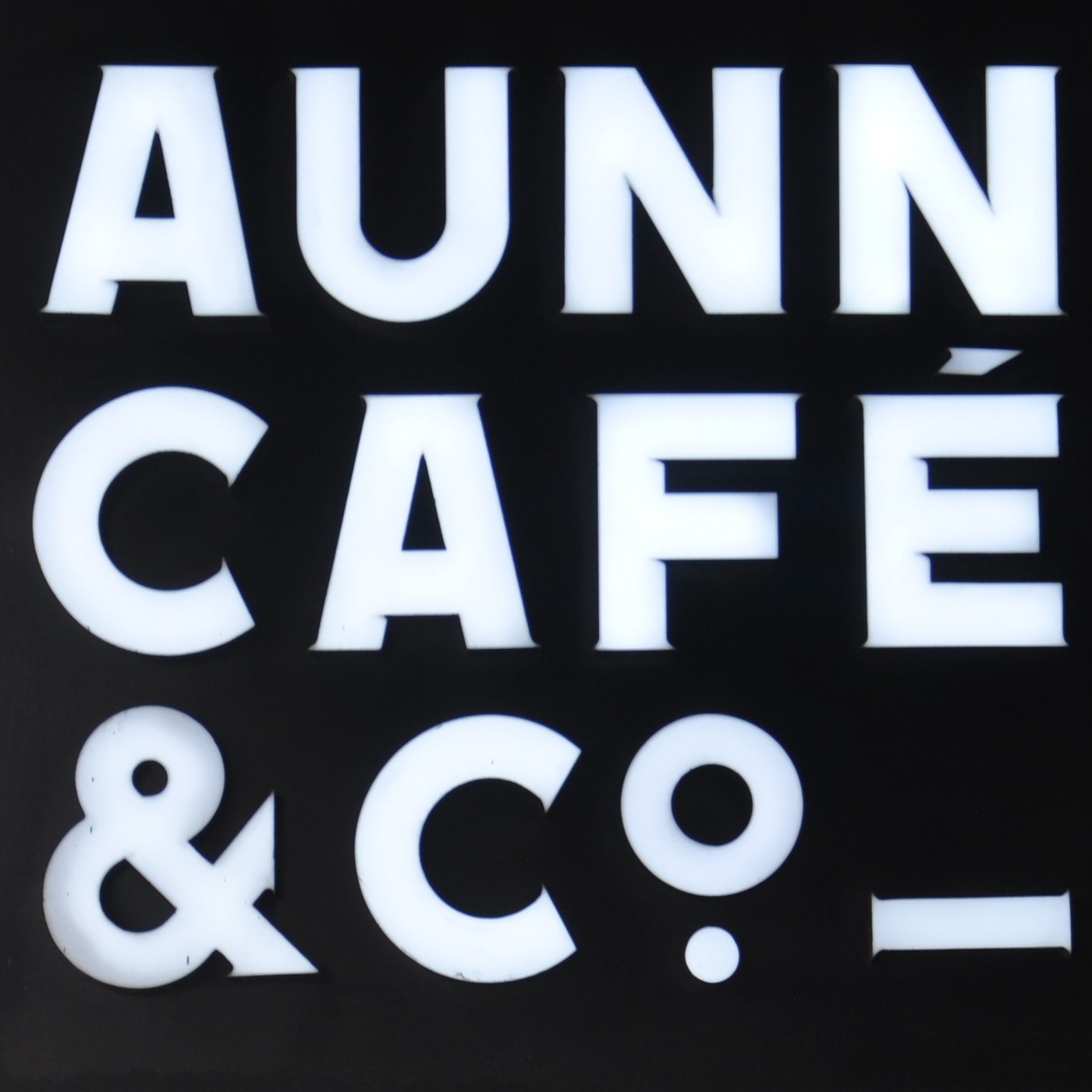The illuminated AUNN CAFÉ & CO. wordmark sign in white letters on black