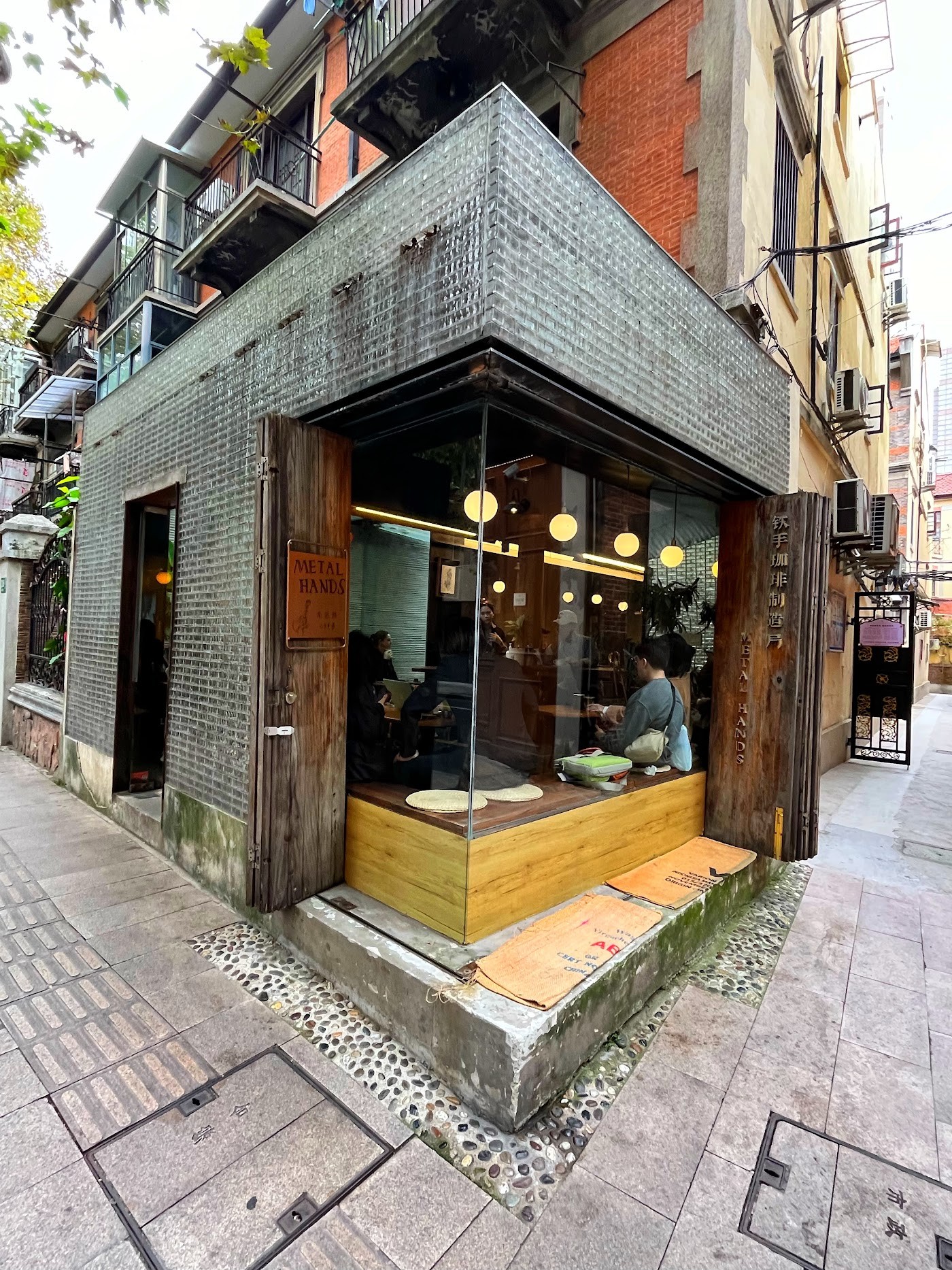 The tiled corner exterior of Metal Hands with its wooden Metal Hands sign and warm lit windows on a Nanchang Road corner