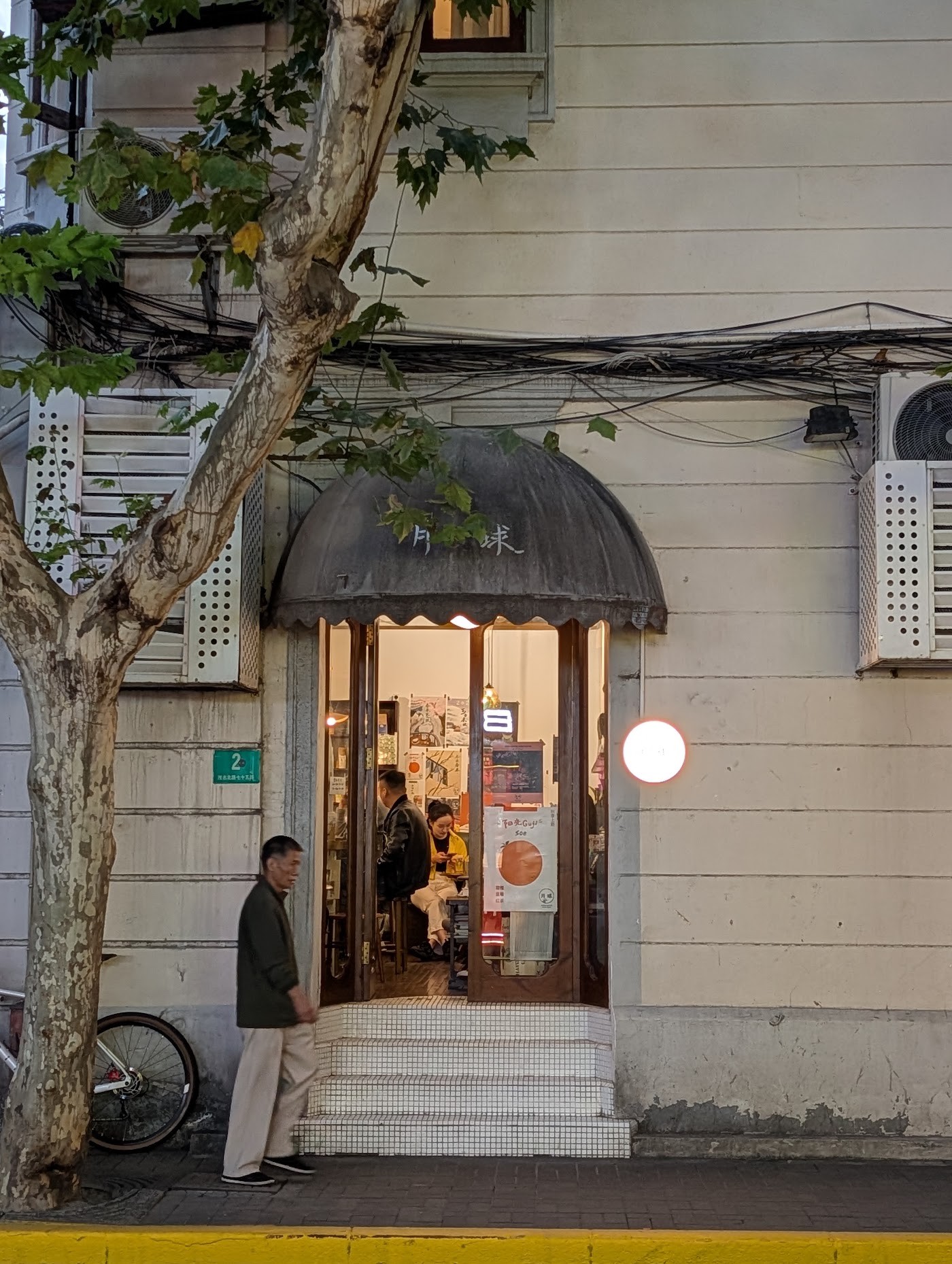 The domed awning entrance to Moon Coffee lit warmly at dusk, tucked beneath a plane tree on a quiet Shanghai lane