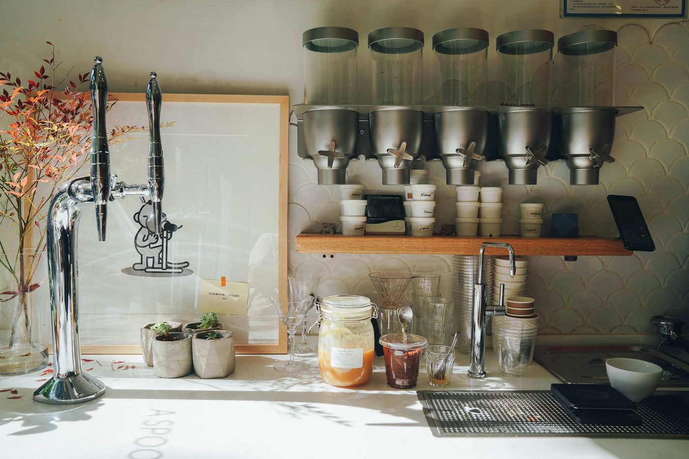 The house made syrup and nitro tap bar at O.P.S. Cafe, with steel dosing hoppers, glassware, and autumn branches on the counter
