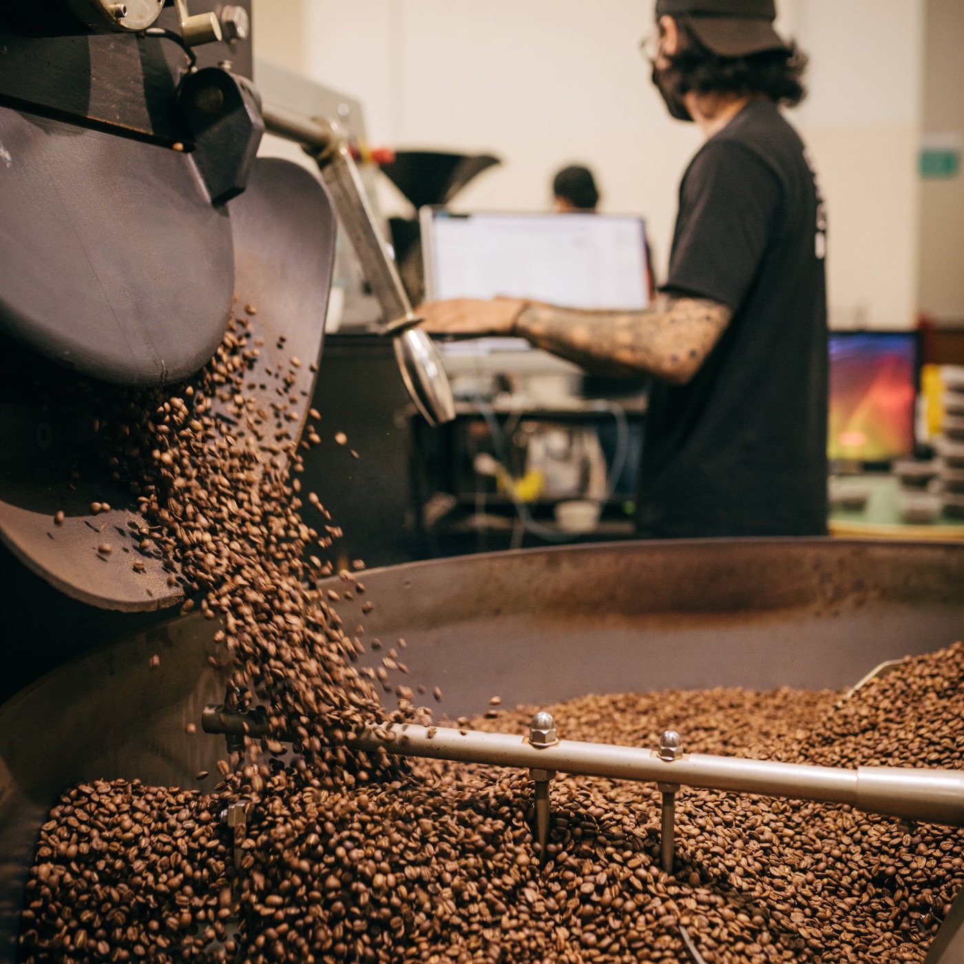 Freshly roasted coffee beans pouring from a roaster into a cooling tray at Common Man Coffee Roasters